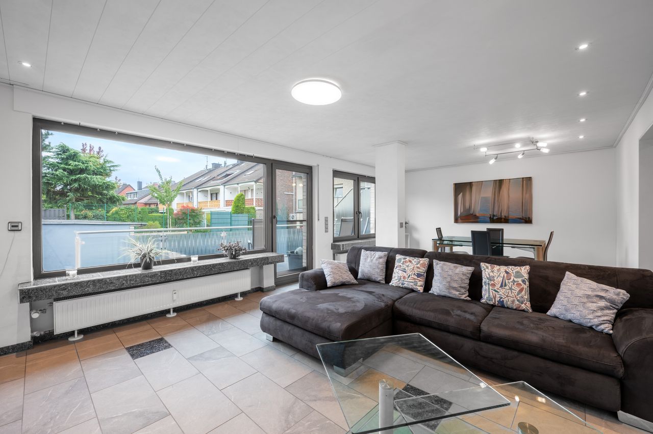 Fully furnished ground floor apartment with 2 rooms, light-filled living/dining area, separate kitchen, large terrace, lawn, and garage in a well-maintained 3-family house.