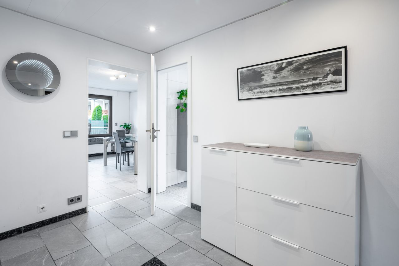 Fully furnished ground floor apartment with 2 rooms, light-filled living/dining area, separate kitchen, large terrace, lawn, and garage in a well-maintained 3-family house.